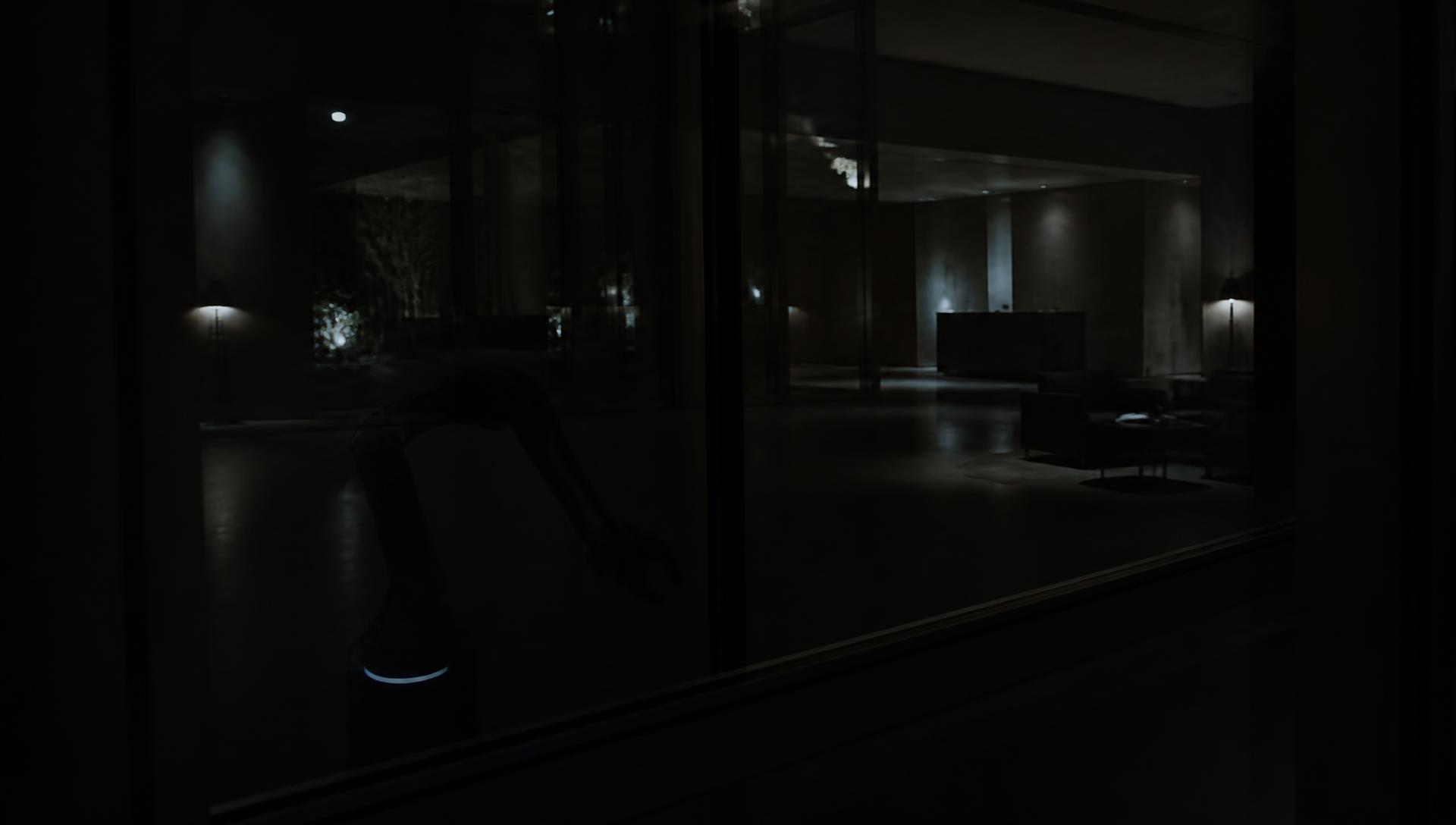 Night view through glass into a quiet hotel lobby with a service machine silhouette